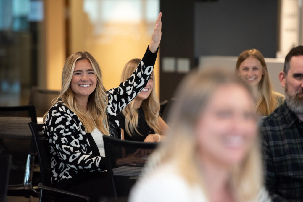 Smiling Turnberry professional raises her hand in mixed colleague co-working space at Turnberry's modern offices
