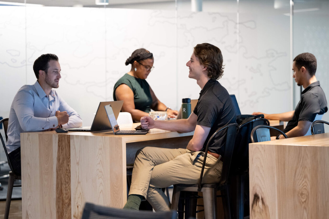 Four young professionals meet in Turnberry's modern offices and work on laptop computers
