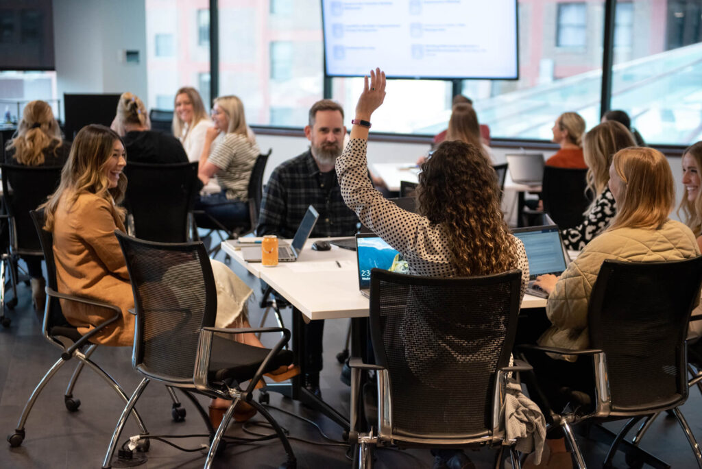 A young professional raises her hand in a group meeting setting at Turnberry's modern office