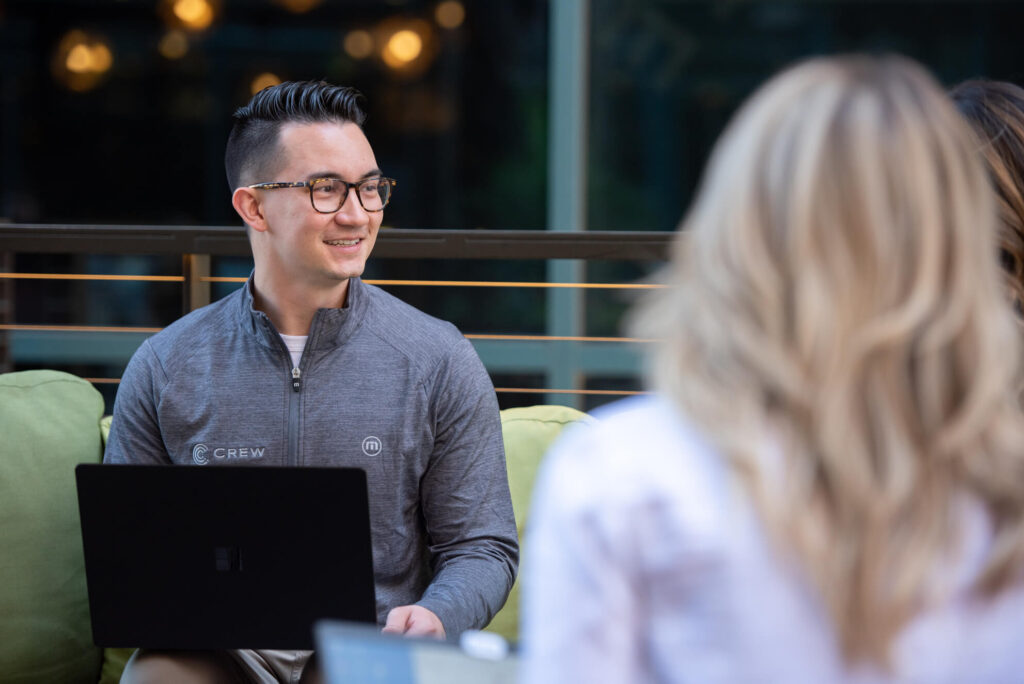 A Turnberry Crew member with a laptop on his lap listens to other colleagues out of view of the image