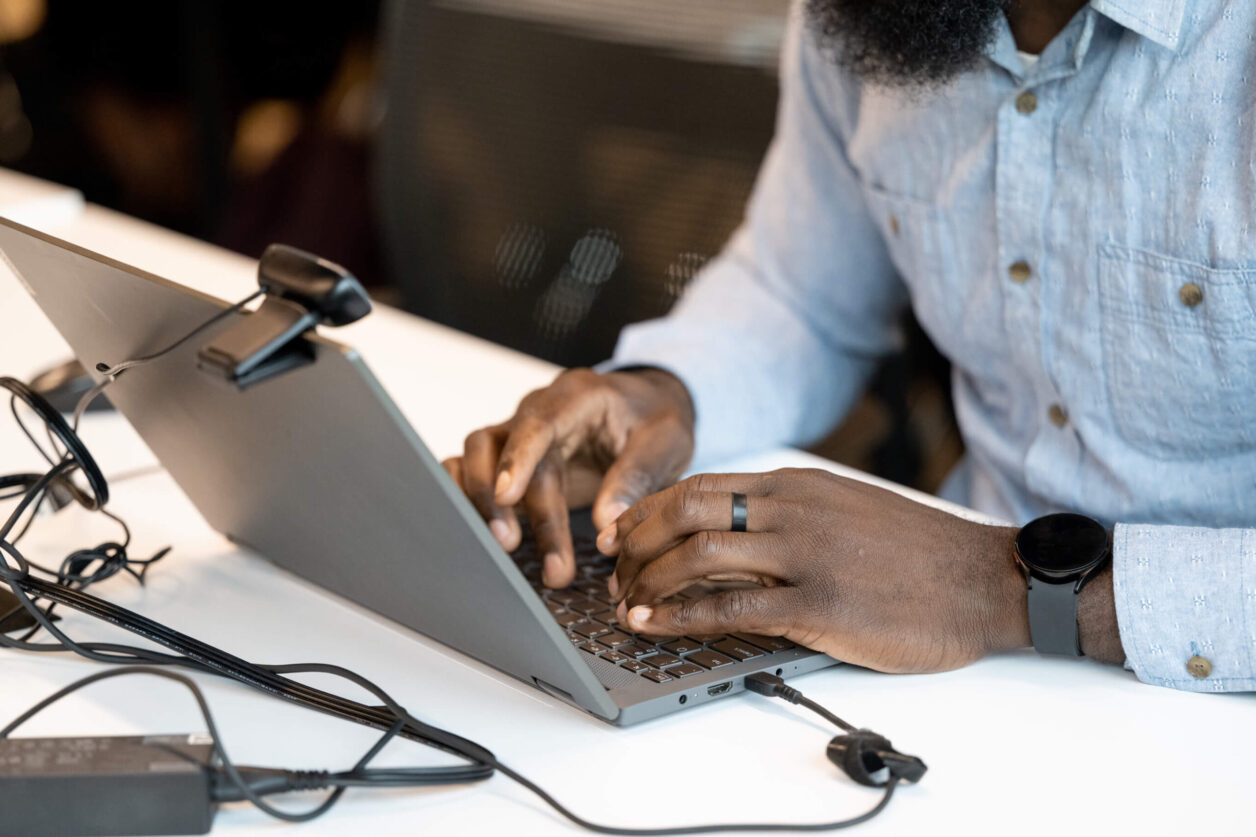 African American man's hands type on a laptop connected to a web camera