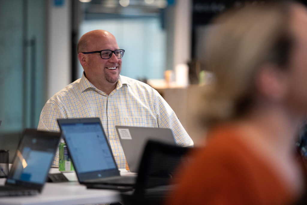 Mature professional smiles while meeting with colleagues in Turnberry's modern, open office space