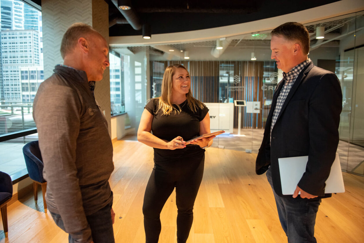 Two mature male colleagues stand with a mid career female professional at Turnberry's offices