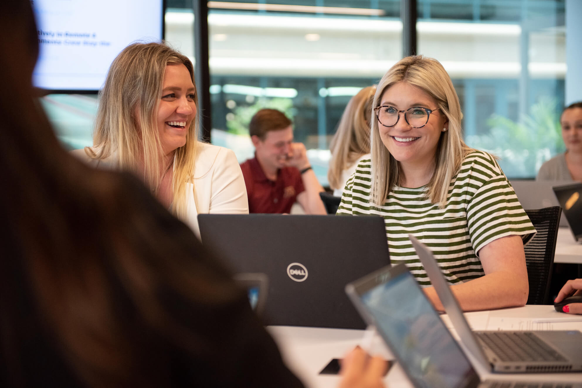 Two professional women smile while meeting with colleagues in Turnberry's modern open coworking space