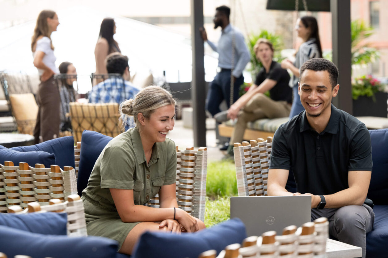 Two young professionals smiling while viewing laptop in Turnberry's outdoor space