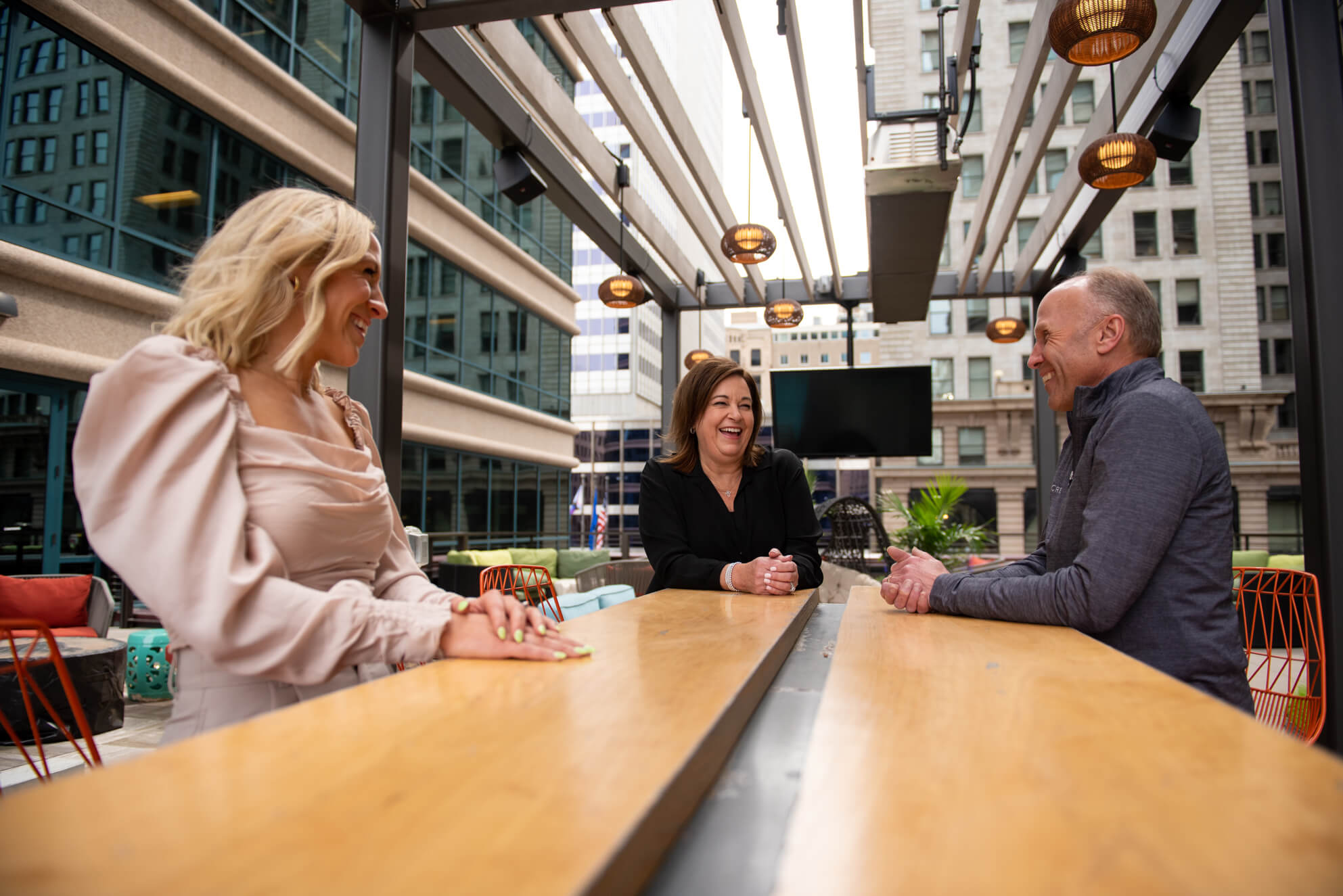 Three middle to mature career professionals laugh together while standing at one of Turnberrry's outdoor meeting tables in downtown Minneapolis, Minnesota