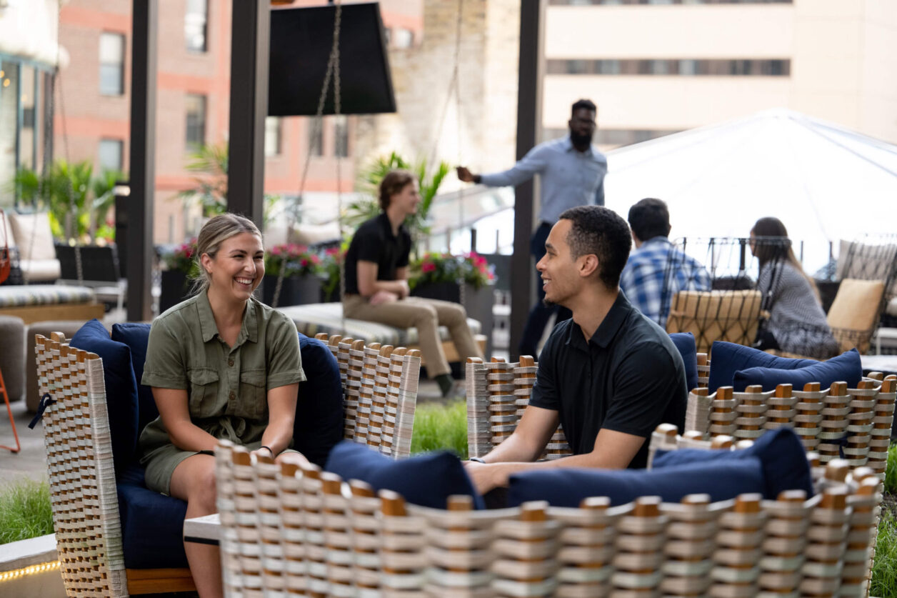 Two groups of young professionals meet in Turnberry's garden space seated in indoor/outdoor furniture