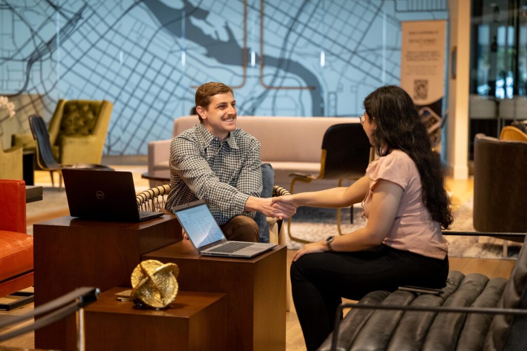 A young male professional shakes hands with a young female professional at Turnberry's casual, modern offices