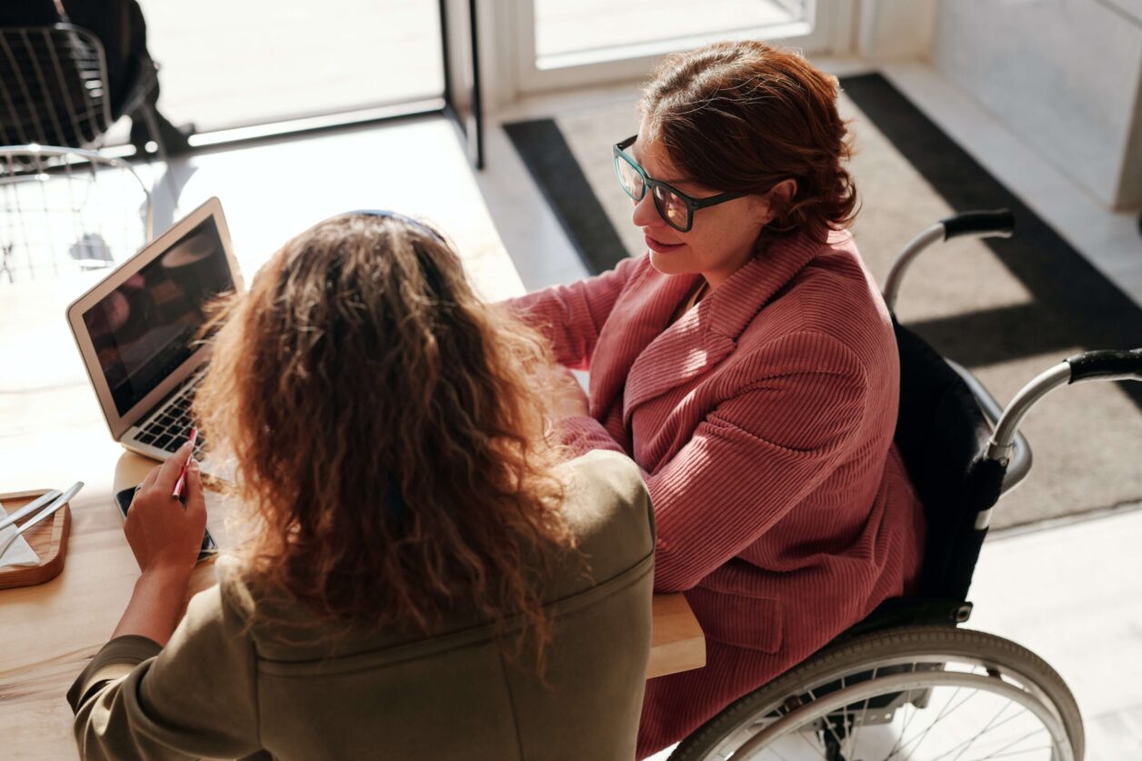 Two female professionals meet in a modern office, one woman is in a wheelchair