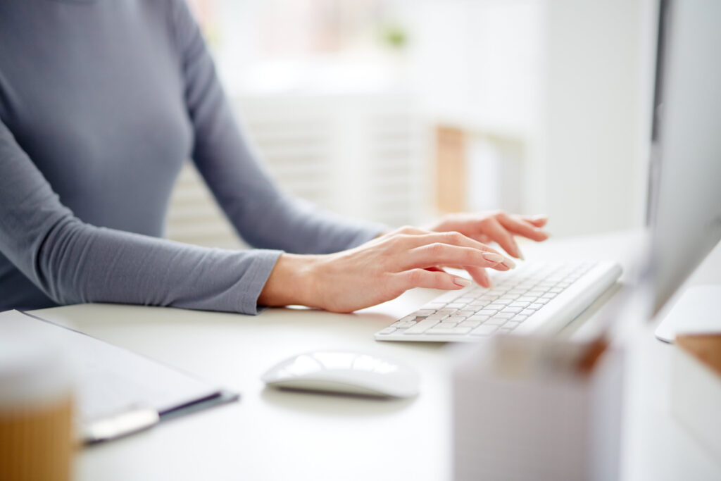Caucasian woman's hands typing on a white keyboard in a modern office