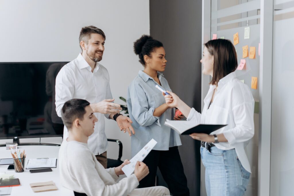 Photo of four mixed level professionals discuss a project using paper and sticky notes