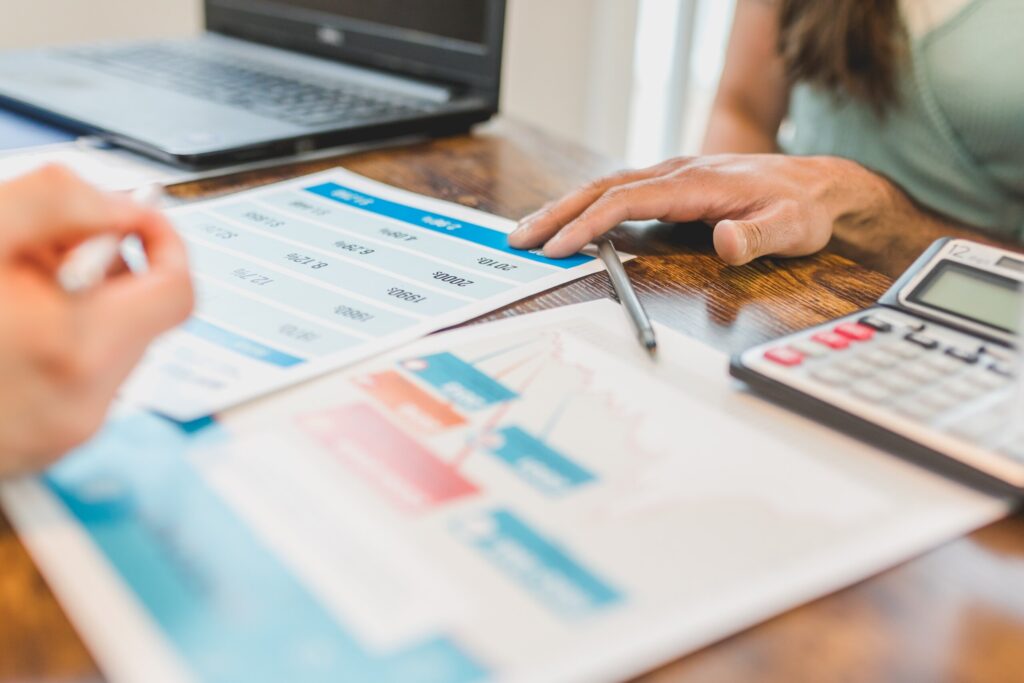 Client and professional hands placed on analysis documents on desk among analog calculator, laptop, and a pen