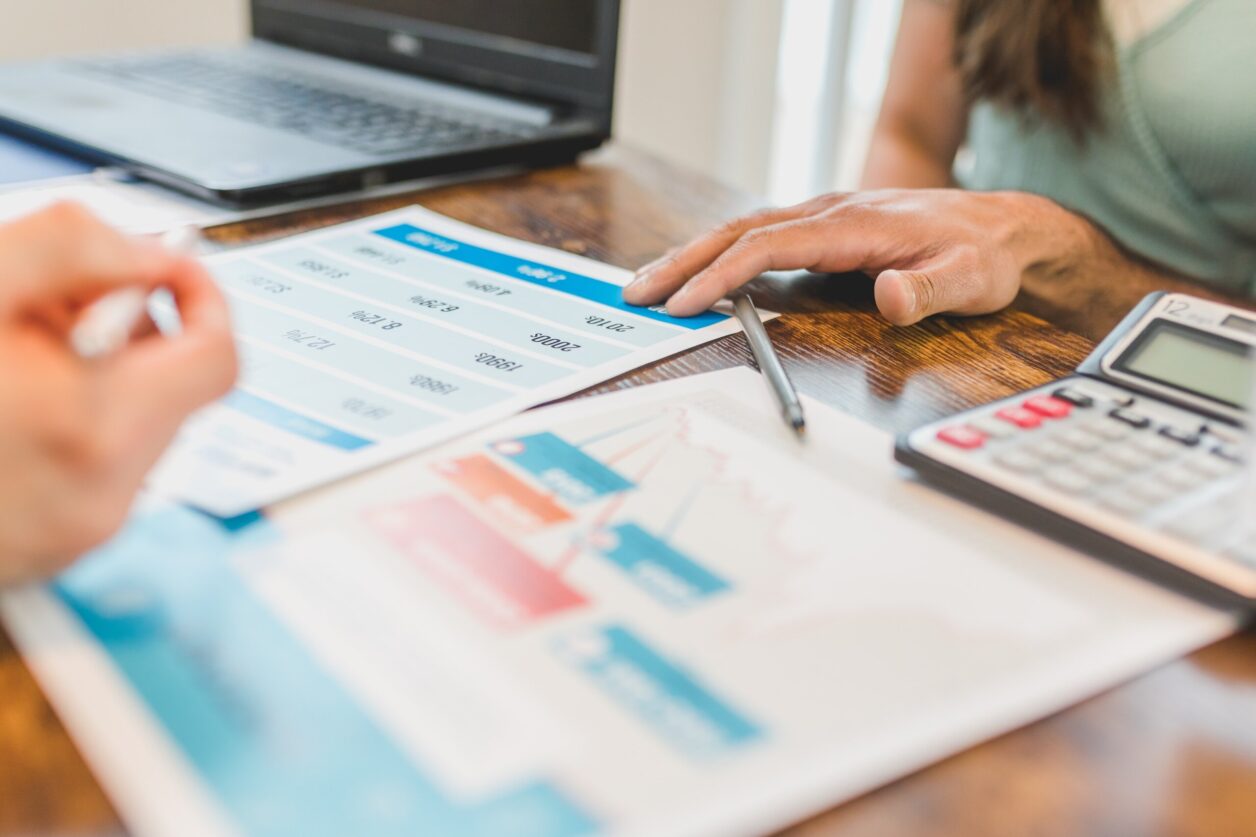 Client and professional hands placed on analysis documents on desk among analog calculator, laptop, and a pen