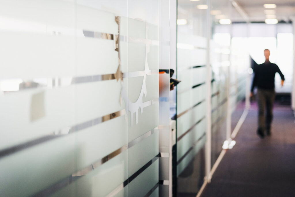 Photograph of man in background walking a hallway lined with glass offices