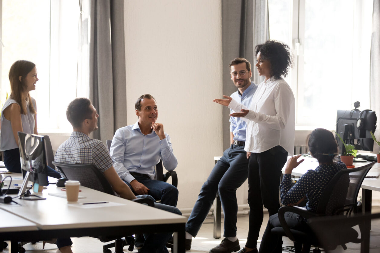 Office professionals listen to a young African American woman present an idea in a modern, open office