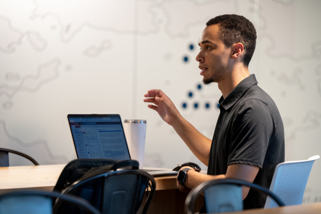 An early career African American man raises a question while sitting behind a laptop at Turnberry's modern Minneapolis office