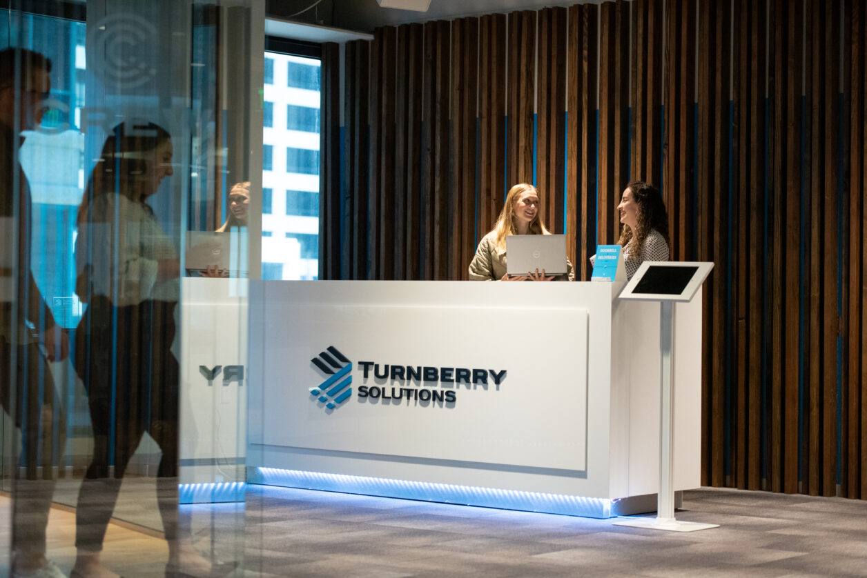 Photograph of Turnberry's lobby with young professionals standing behind branded desk in downtown Minneapolis office