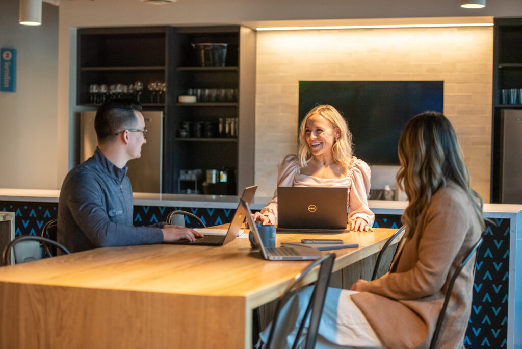 Three early to mid career professionals sit around a table with laptops conversing at Turnberry's modern Minneapolis office