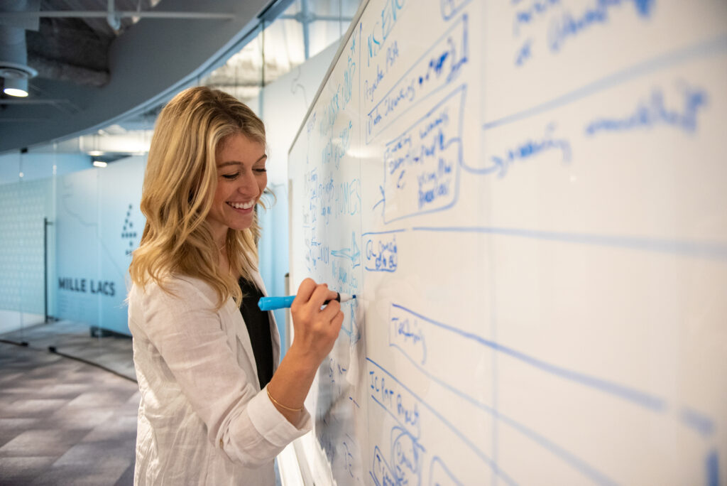 A smiling professional woman writes on a dry erase board