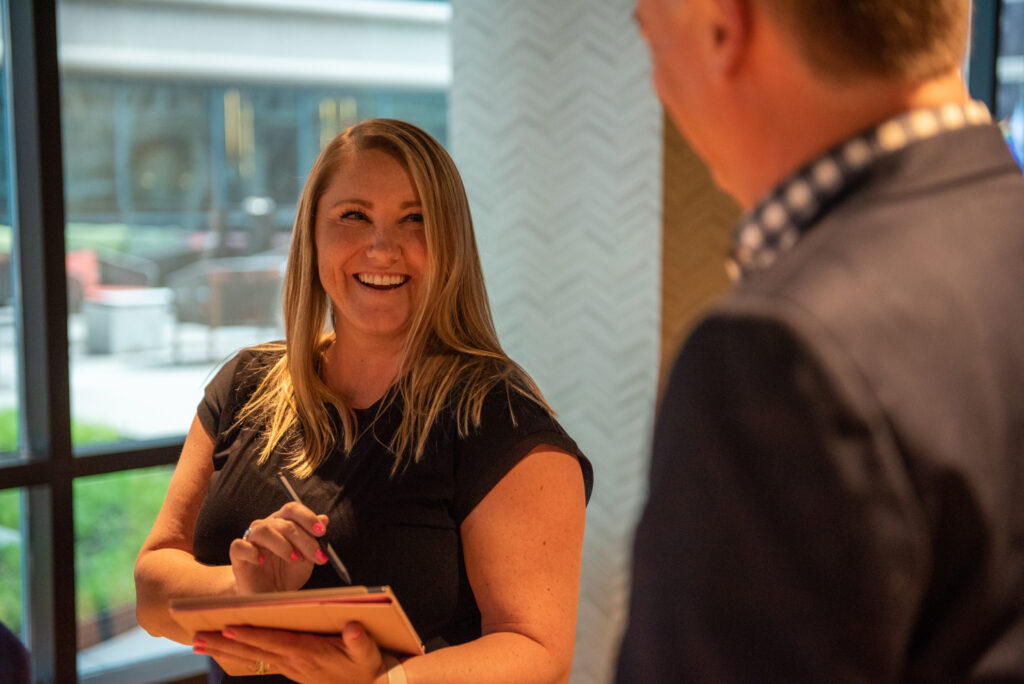 A mid career professional woman smiles at a mature male colleague while holding a notebook and pen in Turnberry's modern Minneapolis office