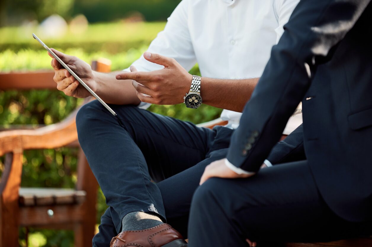 Two seated professionals look at a modern tablet computing device outdoors