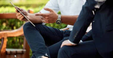 Two seated professionals look at a modern tablet computing device outdoors