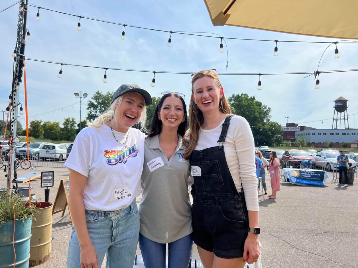 Three female Turnberry professionals pose for a photo at a patio social event featuring Turnberry's Cultural Intelligence group and Shine initiatives